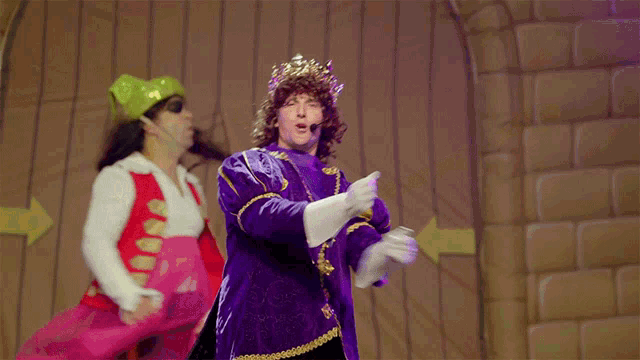 a man in a purple costume with a crown on his head stands on a stage with his arms outstretched