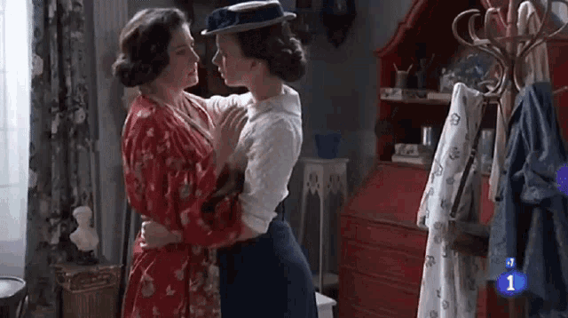 two women are hugging each other in a room with a red dresser .