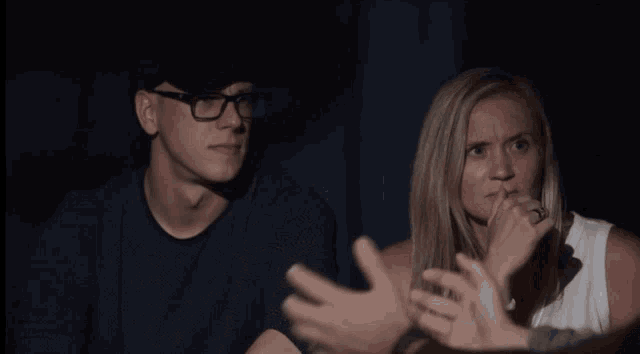 a man and a woman are sitting in a dark room with their hands up
