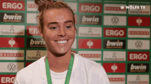 a woman with a medal around her neck is smiling in front of a row of sponsors including ergo and bwin
