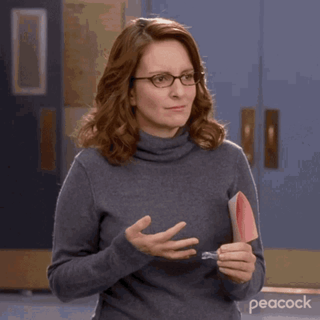 a woman wearing glasses and a turtleneck sweater is holding a piece of paper with the peacock logo on it
