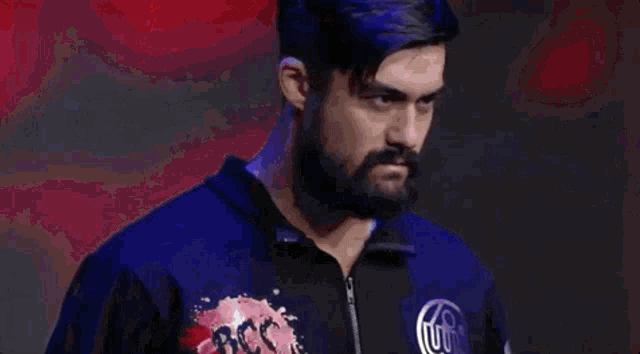 a man with a beard is wearing a blue jacket and standing in front of a red and white flag .