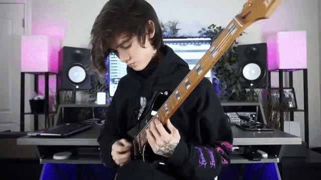 a young man in a black hoodie is playing a guitar