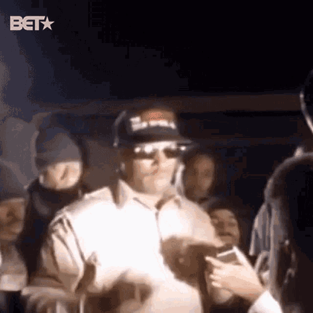 a man wearing sunglasses and a hat is standing in a crowd of people .