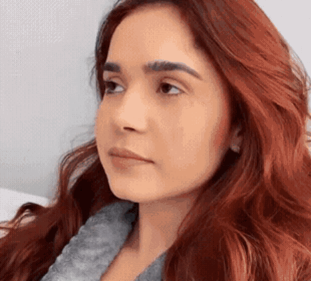 a woman with red hair is wearing a gray sweater