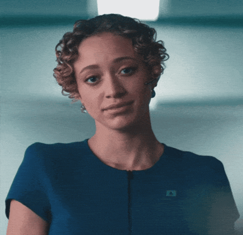 a woman with curly hair wears a blue shirt with a badge that says ' a ' on it