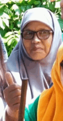 a woman wearing glasses and a hijab is holding a stick