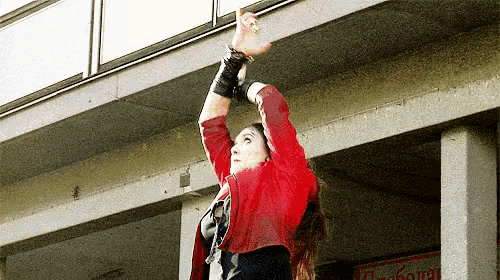 a woman in a red jacket is standing in front of a building and pointing up .