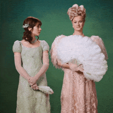 a woman in a pink dress is holding a fan next to another woman in a green dress