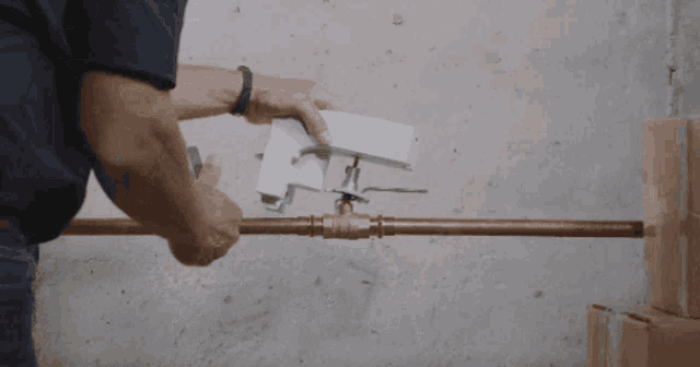 a man is working on a copper pipe and holding a white box