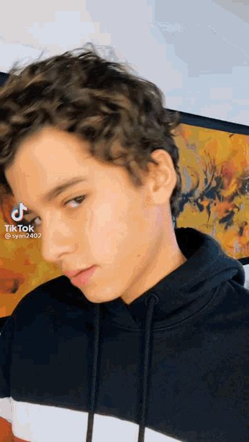 a young man with curly hair is wearing a black hoodie and a tik tok video