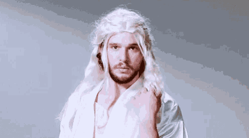 a man wearing a white wig and a white robe is standing in front of a gray background .