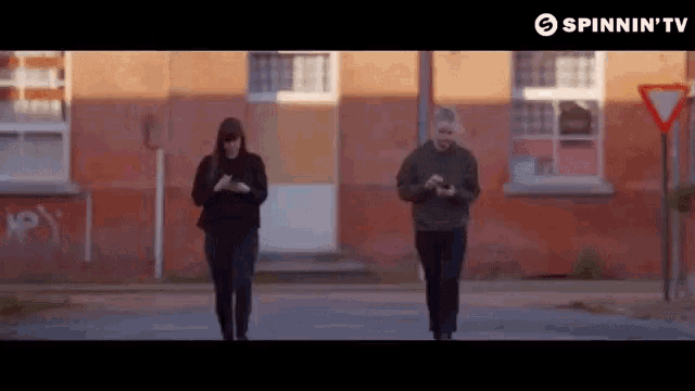 two people walking down a street with a sign that says spinnin ' tv on it