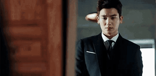 a man in a suit and tie is standing in front of a door and looking at the camera .