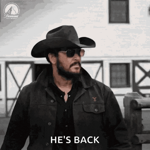 a man wearing a cowboy hat and sunglasses is standing in front of a building and saying `` he 's back '' .