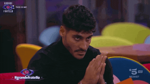 a man sitting in front of a sign that says " grande fratello "