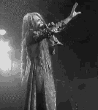 a black and white photo of a woman singing into a microphone on stage .
