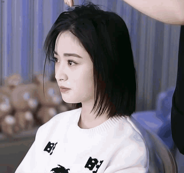 a woman with short black hair is wearing a white sweater