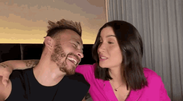 a man with a beard and a woman in a pink shirt are laughing