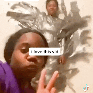 a woman is giving a peace sign in front of a painting of a man wrapped in plastic wrap .