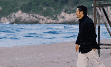 a man in a black jacket walks on a beach