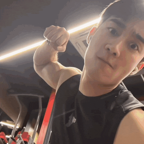 a man in a black tank top is flexing his muscles in a gym