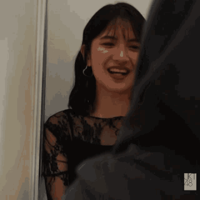a girl in a black lace top is smiling in front of a sign that says jk 48
