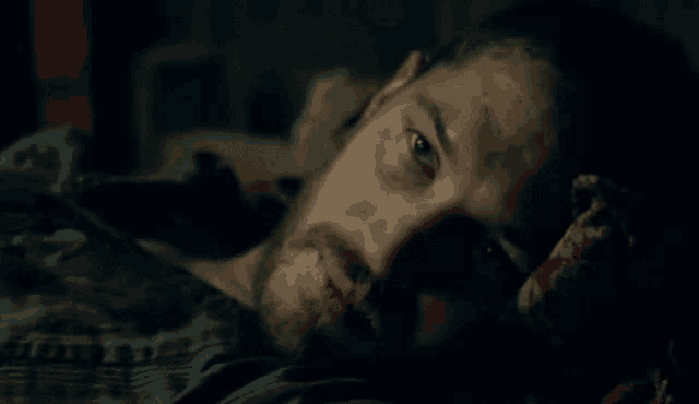 a man with a beard is laying on a bed in the dark .