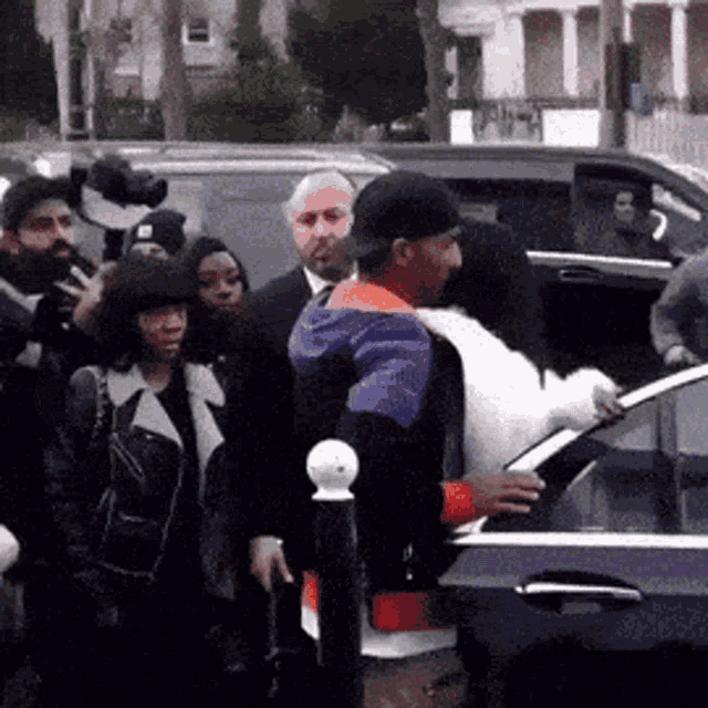 a man in a purple and orange jacket is getting out of a car surrounded by people