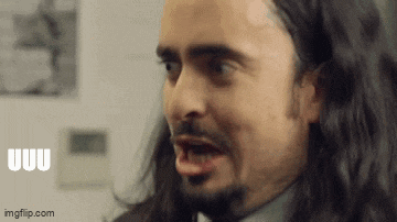 a man with long hair and a beard is making a funny face while wearing a suit and tie .