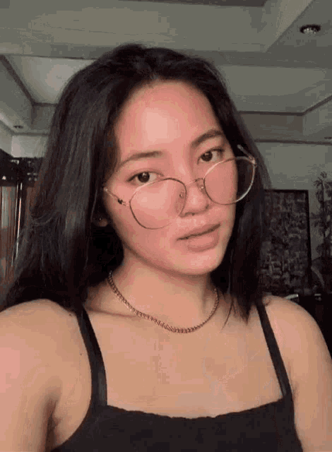 a woman wearing glasses and a black tank top looks at the camera