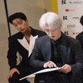 a man in a suit is looking at a piece of paper while sitting next to another man in a suit .