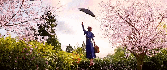 a woman in a blue dress is holding a black umbrella in a garden