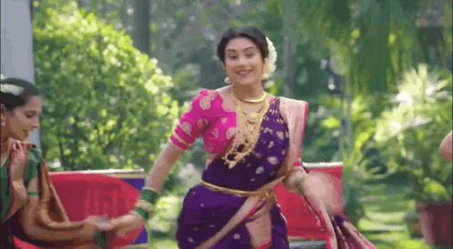 a woman in a purple saree is dancing in a park with other women .