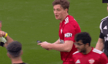 a man in a red shirt that says tables is standing on a soccer field
