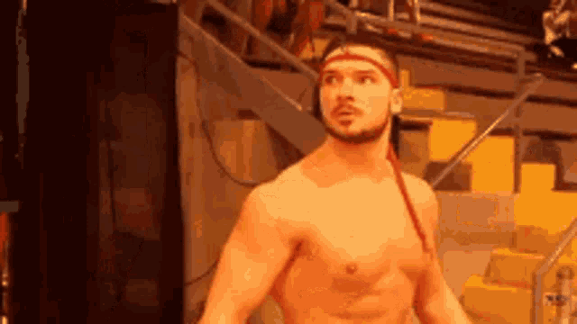 a shirtless wrestler with a red headband is standing in front of a staircase .