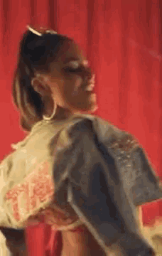 a woman is standing in front of a red curtain wearing a denim jacket and earrings .