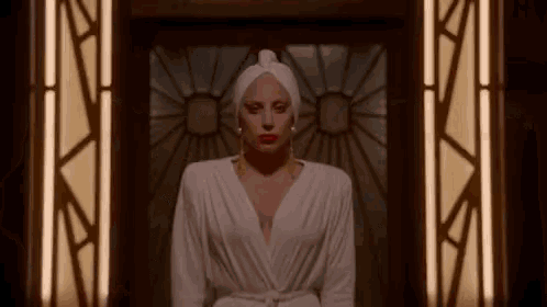 a woman in a white dress and a white towel on her head is standing in front of a stained glass door .