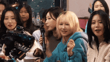 a woman in a blue sweater holds a microphone in front of a group of people