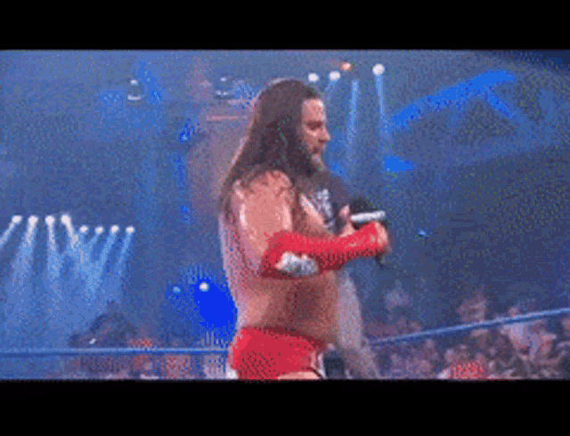 a wrestler in a red outfit is holding a microphone in his hand
