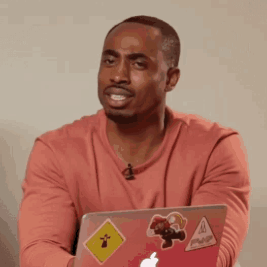 a man wearing a pink shirt is holding an apple laptop with stickers on it