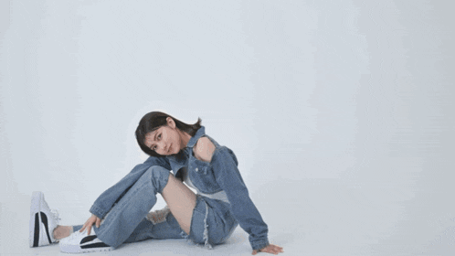 a woman in a denim jacket and ripped jeans is sitting on the floor