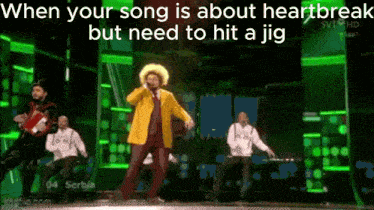 a man in a yellow jacket is singing into a microphone on stage .