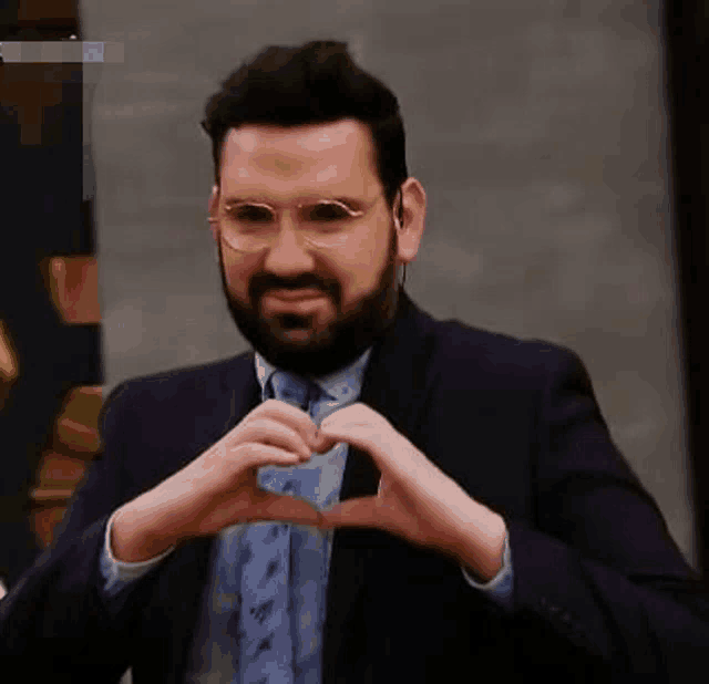 a man in a suit and tie making a heart shape with his hands .