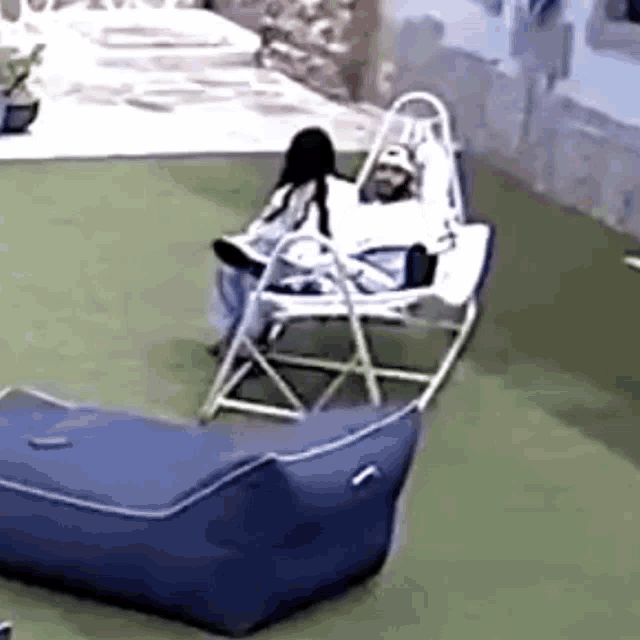 a man and a woman are sitting in a rocking chair on a lawn .