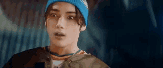 a young man wearing a blue beanie and a green jacket is looking at the camera with a surprised look on his face .