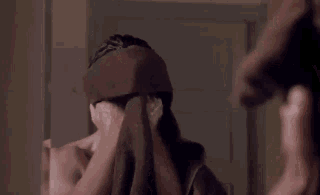 a man is looking at himself in the mirror while holding a towel over his face .