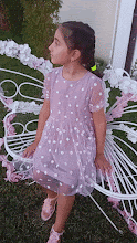 a little girl in a purple dress is standing in front of a butterfly wing .