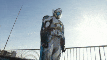 a man in a superhero costume stands on a balcony with the sun shining behind him