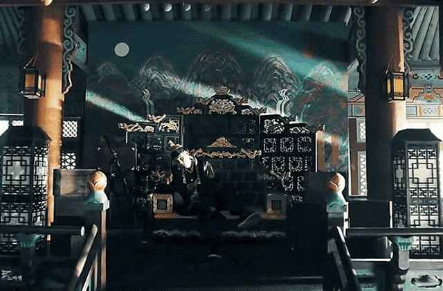 a man sits on a throne in a room with a painting of mountains on the wall